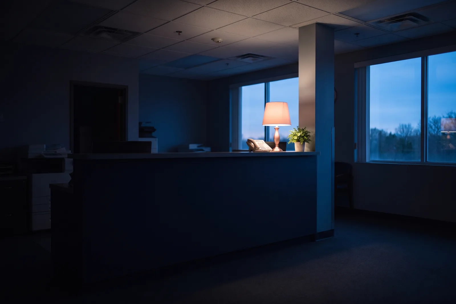 An empty clinic front desk at dusk, the phone under a single warm lamp